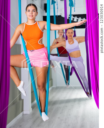 Young girl doing exercises with suspended hammock in aerial yoga studio 123030914