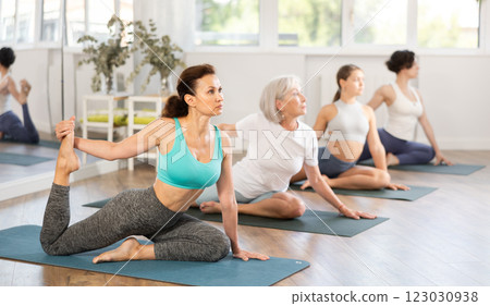 Group of women practicing yoga, working out doing version of Eka Pada Hasta Marjariasana in studio 123030938