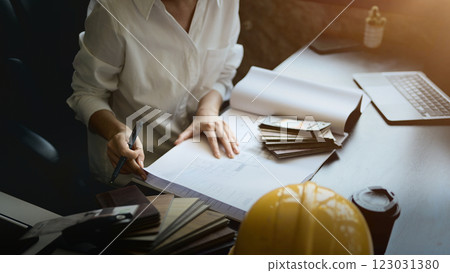 A close-up of a female architect works at her desk, reviewing a building blueprint. 123031380