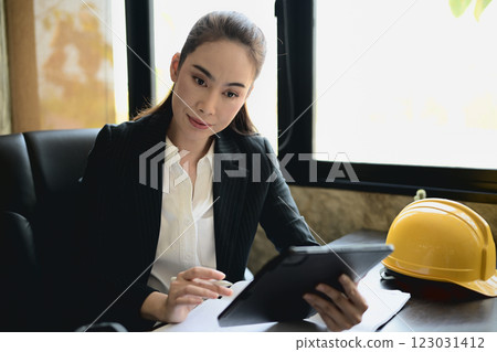 A successful Asian female engineer boss reviewing her project on a digital tablet. A successful Asian female engineer boss reviewing her project on a digital tablet. 123031412