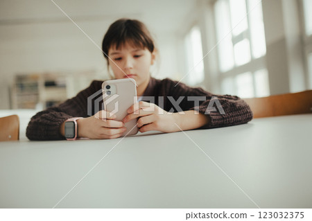 Young schoolgirl sitting in a science lab with a phone in her hand, waiting for classmates. Young schoolgirl sitting in a science lab with a phone in her hand, waiting for classmates. 123032375