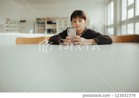 Young schoolgirl sitting in a science lab with a phone in her hand, waiting for classmates. Young schoolgirl sitting in a science lab with a phone in her hand, waiting for classmates. 123032376