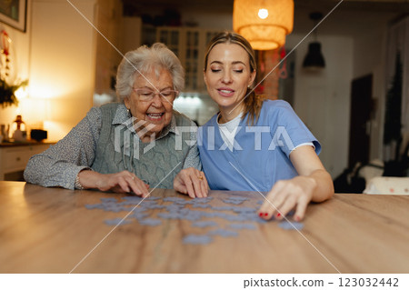 Friendly caregiver and elderly patient working on puzzle together, having fun. 123032442