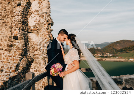 Bride and groom touching by foreheads, looking at each other. Wedding couple standing outside near ruins. Bride and groom touching by foreheads, looking at each other. Wedding couple standing outside near ruins. 123032534