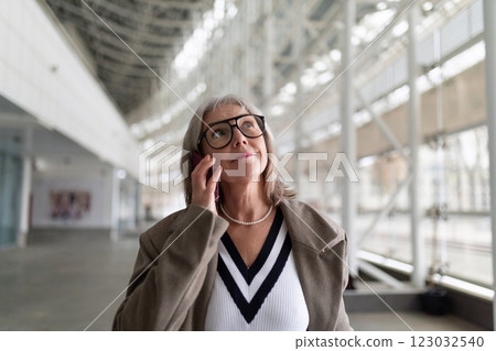 Older woman in a stylish outfit gazes thoughtfully around a modern indoor venue during an afternoon 123032540