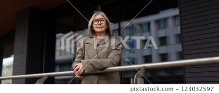 Stylish elderly woman enjoying a sunny day outside a modern building while leaning on a railing in Stylish elderly woman enjoying a sunny day outside a modern building while leaning on a railing in 123032597