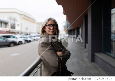 Senior businesswoman standing confidently on a city street, dressed in a stylish coat while enjoying 123032598