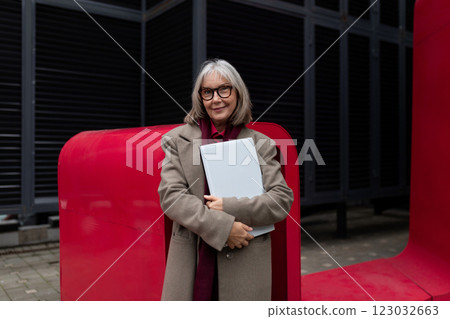Elderly businesswoman confidently standing outside her office, holding a folder, surrounded by Elderly businesswoman confidently standing outside her office, holding a folder, surrounded by 123032663