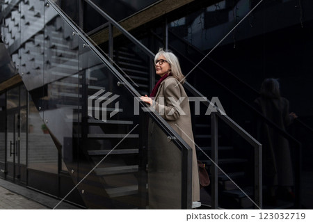 Stylish elderly woman with gray hair ascends modern staircase in a city setting during the daytime Stylish elderly woman with gray hair ascends modern staircase in a city setting during the daytime 123032719