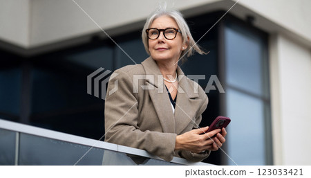 Stylish elderly woman enjoys a moment of reflection while leaning on a balcony railing in an urban 123033421