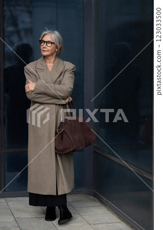 Senior businesswoman confidently standing outside a modern corporate building during daytime Senior businesswoman confidently standing outside a modern corporate building during daytime 123033500
