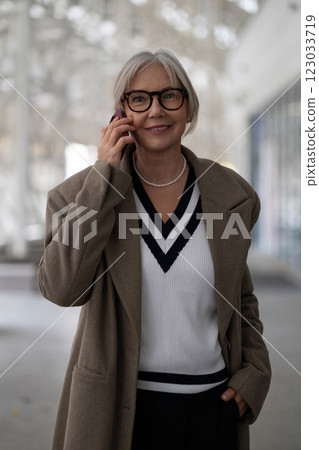 Elderly businesswoman in casual attire conversing on her mobile phone in a modern office space Elderly businesswoman in casual attire conversing on her mobile phone in a modern office space 123033719