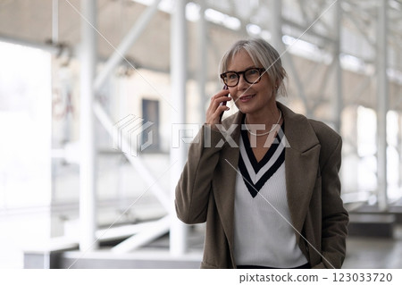 Middle aged businesswoman in stylish coat smiling while talking on the phone in a modern office Middle aged businesswoman in stylish coat smiling while talking on the phone in a modern office 123033720