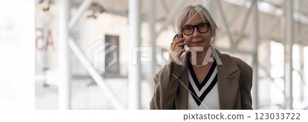 Older woman with glasses talking on the phone while walking in a modern urban setting during the day 123033722
