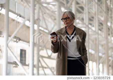 A middle-aged businesswoman checks her smartphone while walking through a modern office building in 123033729