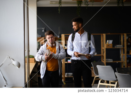 Young man with Down syndrome and his teacher talking while walking down the school hallway. 123034714