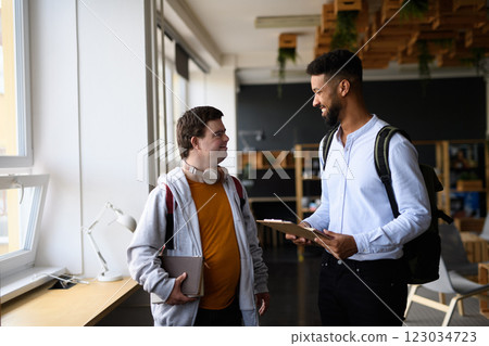 Young man with Down syndrome and his teacher talking while walking down the school hallway. 123034723