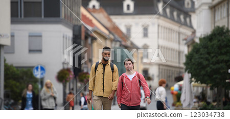 A young man with Down syndrome and his mentoring friend walking across city, talking. A young man with Down syndrome and his mentoring friend walking across city, talking. 123034738
