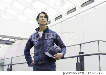 A young male worker wearing denim work clothes and standing with a helmet. Photo courtesy of Sky Perfect Tokyo Media Center. 123035333