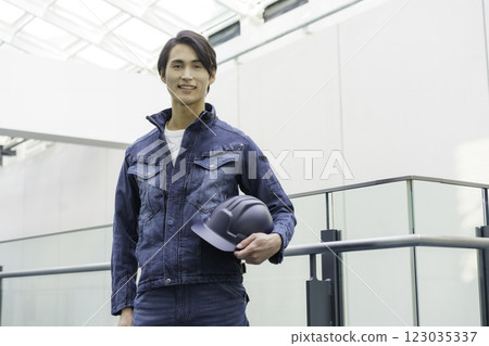 A young male worker wearing denim work clothes and standing with a helmet. Photo courtesy of Sky Perfect Tokyo Media Center. 123035337