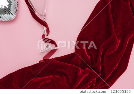 A minimalist and creative composition featuring a wine glass, red velvet fabric, disco heart and ribbon on a soft pink background, representing elegance, celebration, and sophisticated design. 123035393