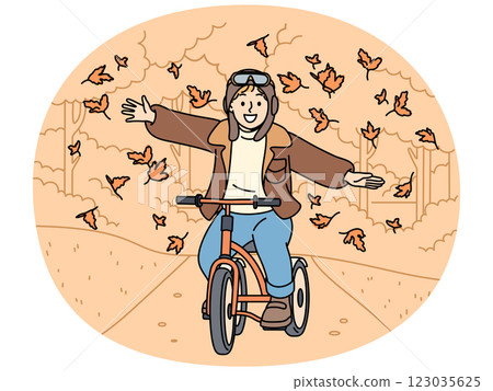 Happy child rides bicycle through autumn park and spreads arms to sides enjoying falling leaves 123035625