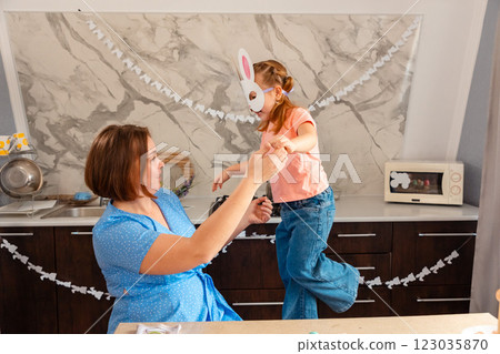 Easter Spring festival. Caucasian Mother plays together with her little happy daughter in rabbit mask, sitting in decorated kitchen 123035870