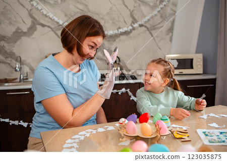 Happy mother and little smiling daughter play together and unpack chocolate eggs for the Easter spring holiday. Caucasian woman with rabbit glove on her hand is playing with a child Happy mother and little smiling daughter play together and unpack chocolate eggs for the Easter spring holiday. Caucasian woman with rabbit glove on her hand is playing with a child 123035875