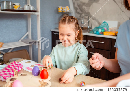 Portrait of Caucasian cute little daughter and her mother are preparing at home for the Easter spring holiday. Festive table and kitchen decoration with handmade decorations 123035879