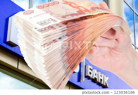 Stack of russian rubles in the hand against the signboard. Text in russian: Bank 123036186