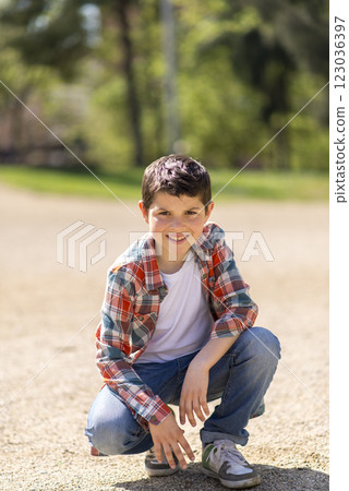 Young boy squatting on a gravel path in a sunny park. Young boy squatting on a gravel path in a sunny park. 123036397