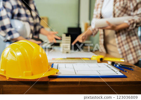 Yellow hard hat on workbench with Construction engineers discussion at construction site. 123036809