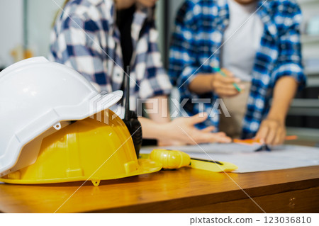 Yellow hard hat on workbench with Construction engineers discussion at construction site. Yellow hard hat on workbench with Construction engineers discussion at construction site. 123036810