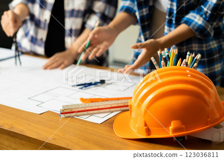 Yellow hard hat on workbench with Construction engineers discussion at construction site. Yellow hard hat on workbench with Construction engineers discussion at construction site. 123036811