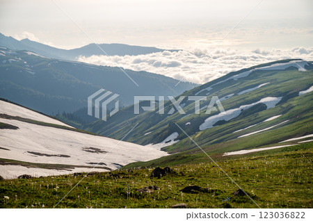 Green mountains with melting snow and fresh grass under cloudy sky. 123036822