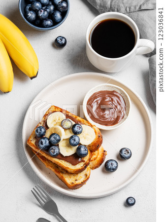 Toasted bread with chocolate cream, blueberries and banana on a plate on a light background Toasted bread with chocolate cream, blueberries and banana on a plate on a light background 123036841