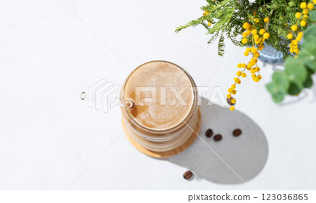 Cold coffee latte or mocha in a glass with milk and ice on a light background with a bouquet of mimosa Cold coffee latte or mocha in a glass with milk and ice on a light background with a bouquet of mimosa 123036865