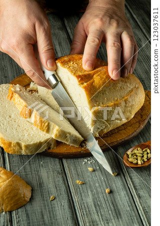 A pair of hands expertly cuts a golden loaf of bread with a sharp knife. The warm, fresh scent fills the air as the crusty exterior reveals a soft interior, perfect for sharing A pair of hands expertly cuts a golden loaf of bread with a sharp knife. The warm, fresh scent fills the air as the crusty exterior reveals a soft interior, perfect for sharing 123037611