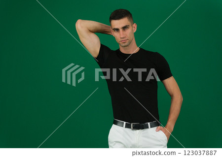 Handsome young man on grey background looking at camera. Portrait of laughing young man with hands in pockets leaning against grey wall. Happy guy smiling. 123037887