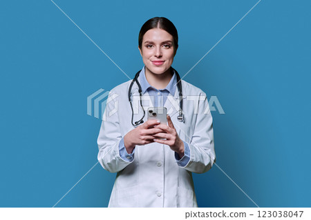 Young female doctor holding smartphone, on blue studio background Young female doctor holding smartphone, on blue studio background 123038047