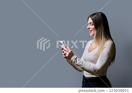 Profile view, young beautiful woman using mobile phone on grey background Profile view, young beautiful woman using mobile phone on grey background 123038051