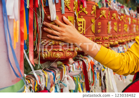 Person pilgrim female hand touching turning spinning Buddhist prayer wheel at Buddhist monastery. Prayer wheels in Buddhist stupa temple. Buddhism religion concept 123038482