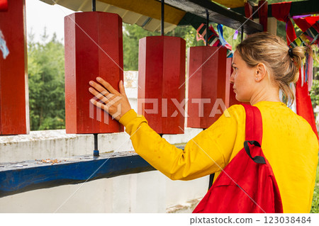 Person pilgrim woman touching turning spinning Buddhist prayer wheel at Buddhist monastery. Prayer wheels in Buddhist stupa temple. Buddhism religion concept 123038484