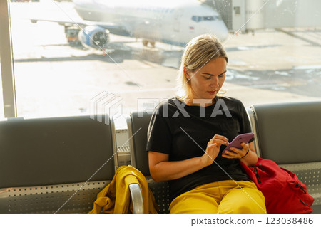 Airport terminal. Woman waiting for flight using smartphone. Girl with cell phone in airport surfing internet social media apps. Traveling female in boarding lounge of airline hub. Traveling girl 123038486