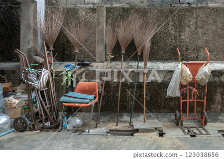 View of Six broomsticks and Three wheelbarrow (Hand truck dolly) with old chair Beside old cement walls background. 123038656