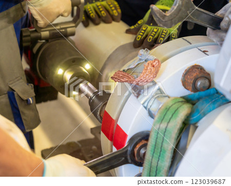 Workers using hydraulic tools and lifting straps to dismantle a flanged pipeline. Workers using hydraulic tools and lifting straps to dismantle a flanged pipeline. 123039687