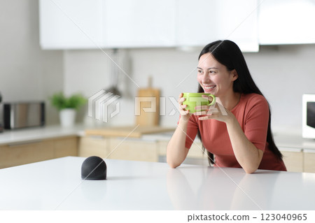 Happy asian woman drinking in the kitchen with smart speaker 123040965