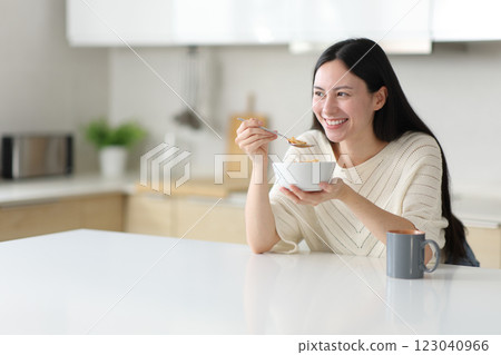 Happy asian woman eating cereals in a kitchen island at home Happy asian woman eating cereals in a kitchen island at home 123040966