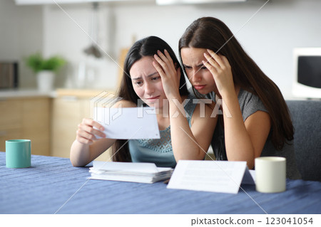 Sad roommates checking bank statement in a kitchen Sad roommates checking bank statement in a kitchen 123041054