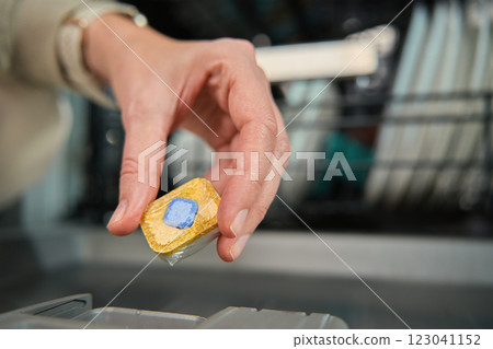 Close-up of female hand placing dishwasher detergent tablet into dispenser compartment. Efficient and hygienic dishwashing 123041152